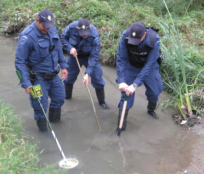 three officers search a stream for evidence